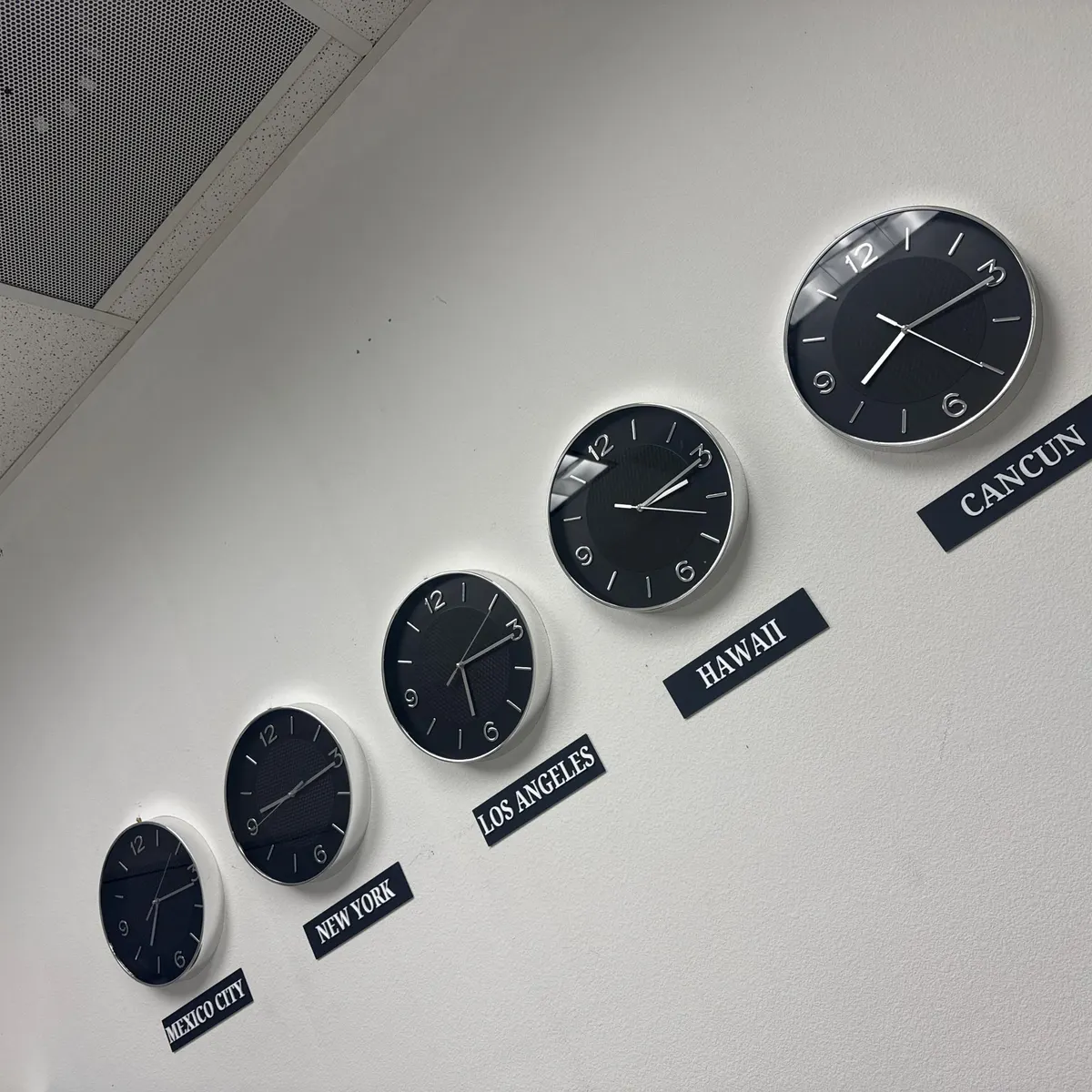Five silver world-time clocks with city signs on an office wall