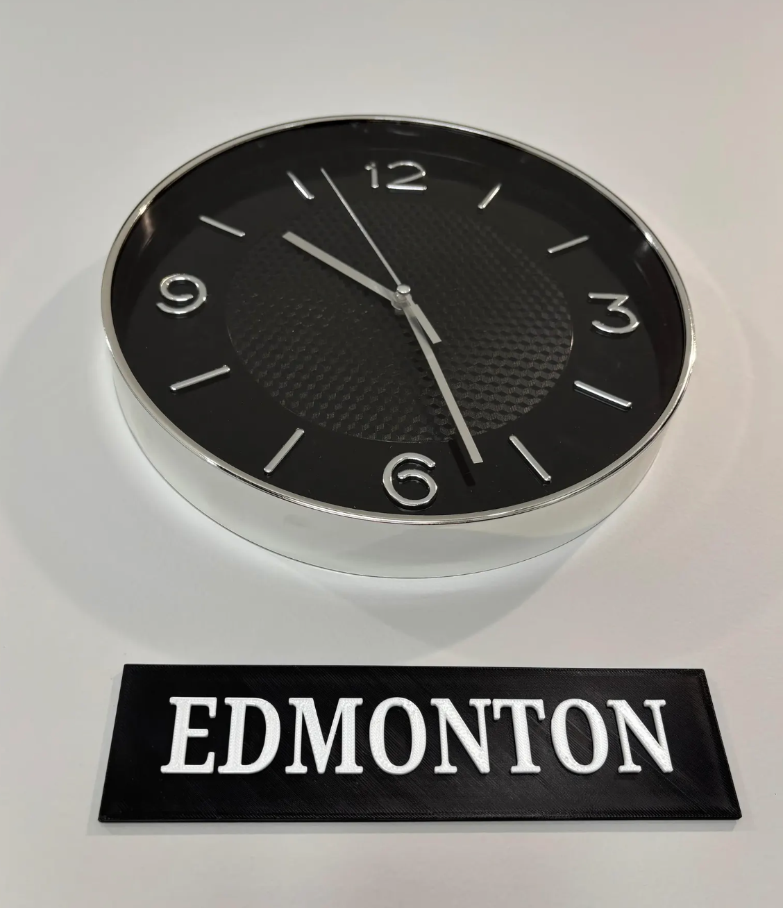Close-up of a chrome clock with an Edmonton city sign